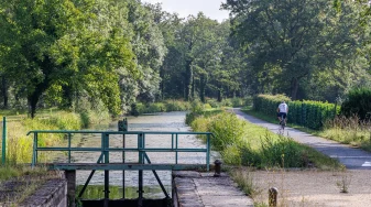 Au premier plan une écluse et sur le chemin de halage un cyclotouriste de dos